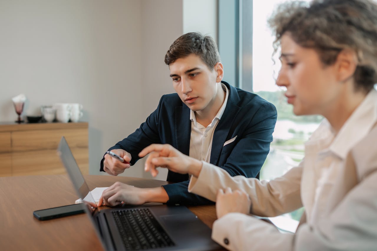 Two professionals collaborating on a laptop while reviewing Anglais Juridique materials in an office setting.